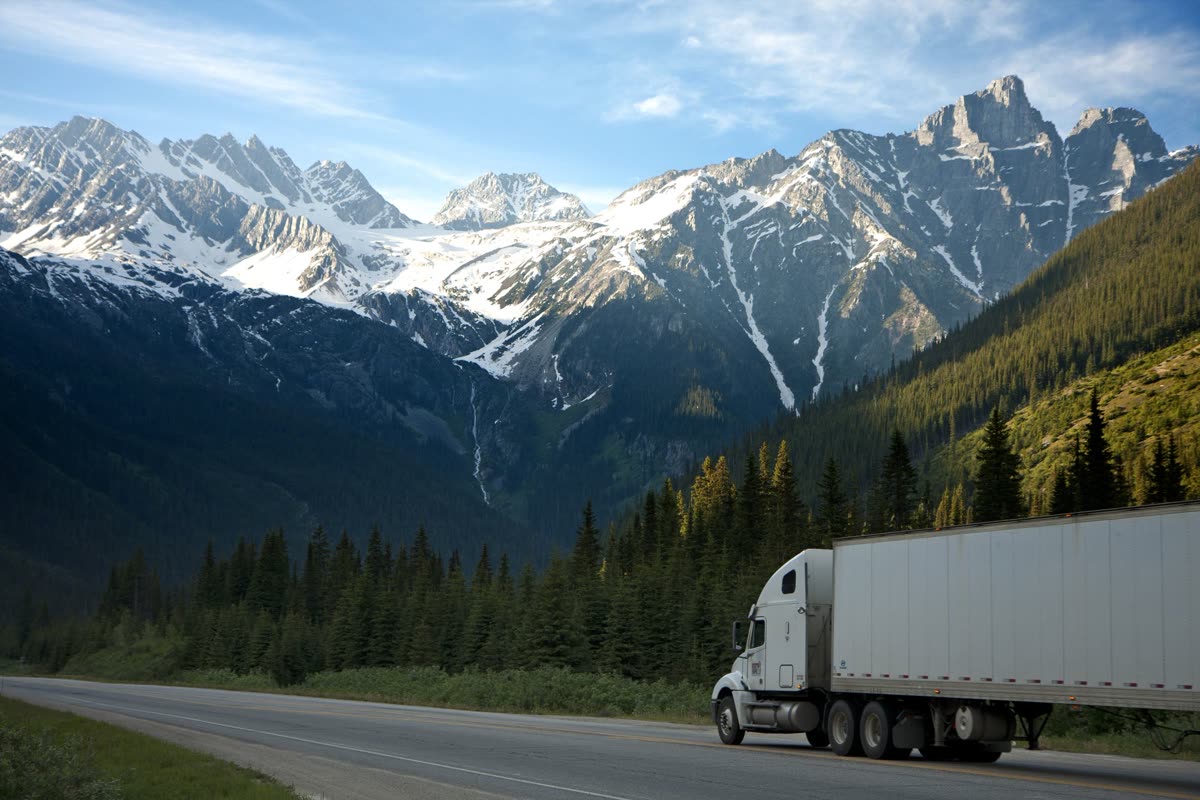 Unbranded white tractor-trailer traveling an interstate highway through mountains