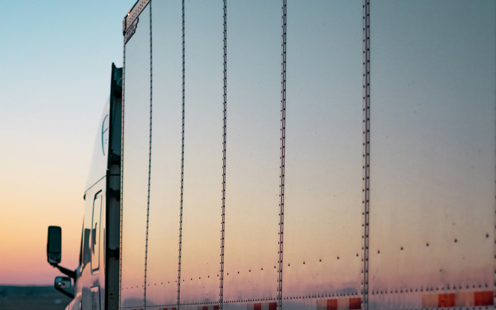 Side of an unbranded Class 8 tractor-trailer on the highway at dusk
